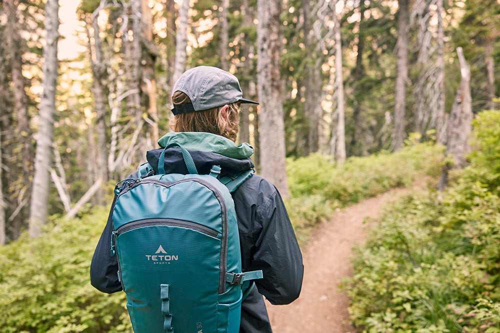 Man stands on trail with backpack in woods.