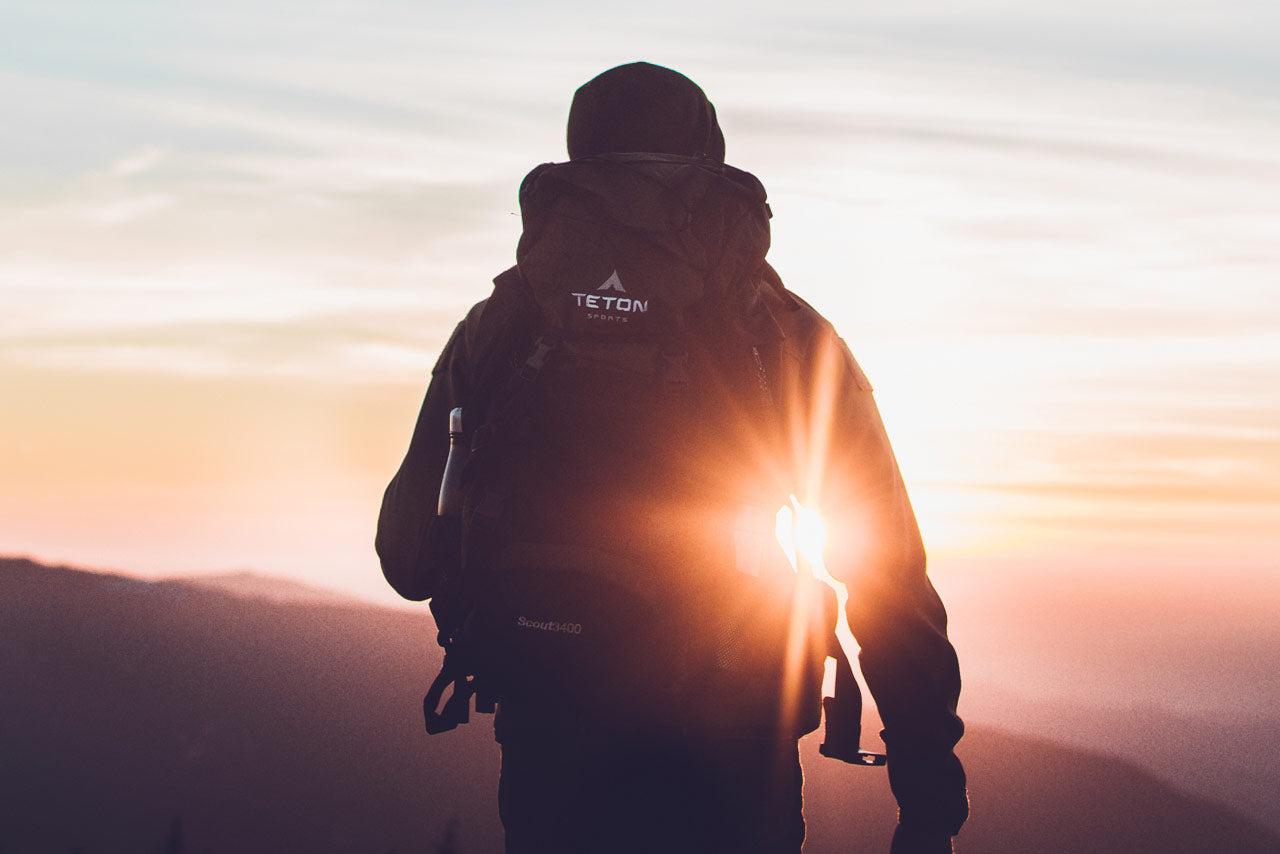 Man looks out at sunset with backpack.