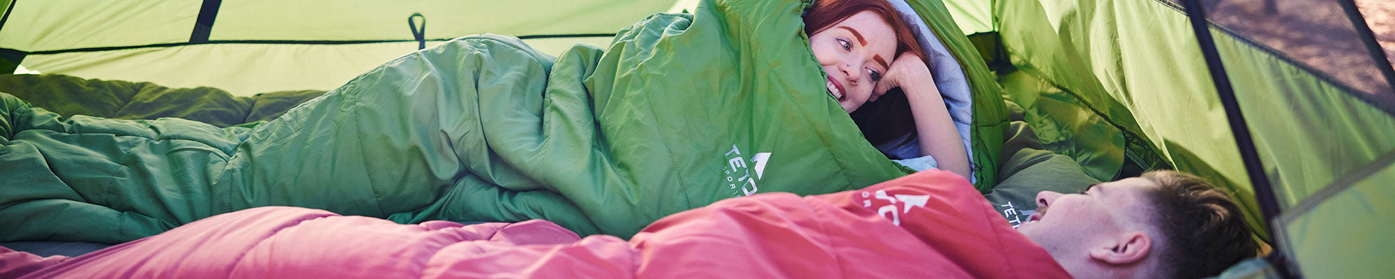 A couple snuggles up in their TETON Sports mummy sleeping bags.