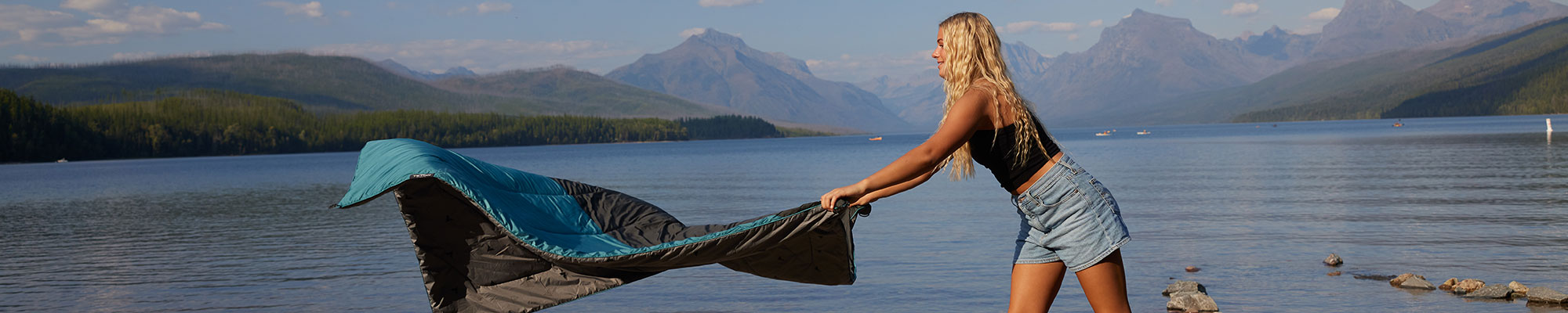 A woman laying out her blanket by a lake.