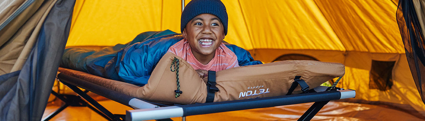 A young boy lays on his TETON Sports Adventurer cot and camp pad while inside a Sierra Canvas Tent.