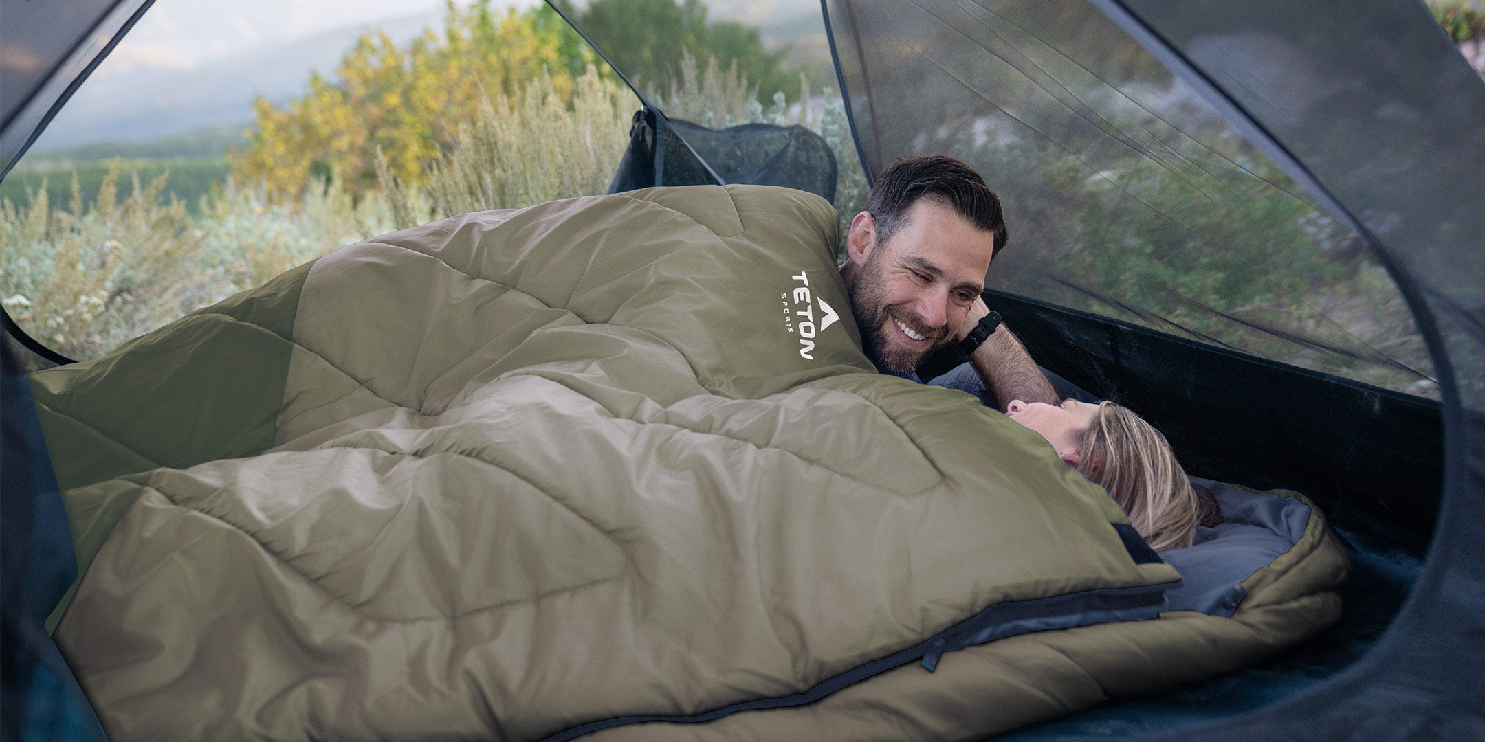 A couple snuggles together in a TETON Sports Celsius Mammoth Sleeping Bag.
