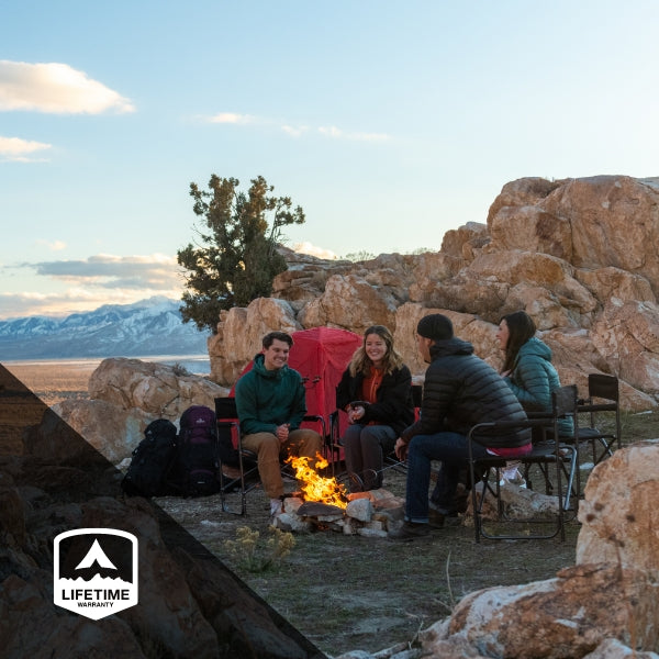 TETON Sports Lifetime Warranty: Image shows four friends hanging out around a campfire, laughing together. They are surrounded by red rocks and there is TETON Mountain Ultra tent in the background.