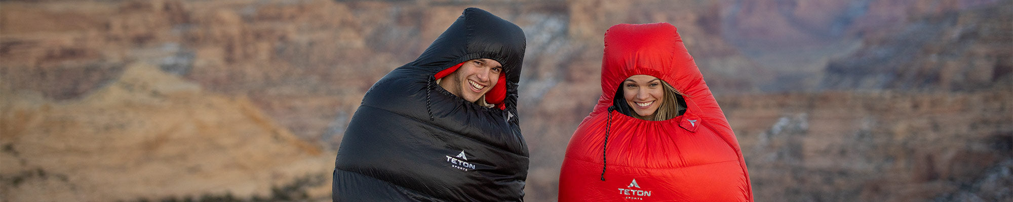 A couple poses together while wearing TETON Sports ALTOS Mummy Sleeping Bags.