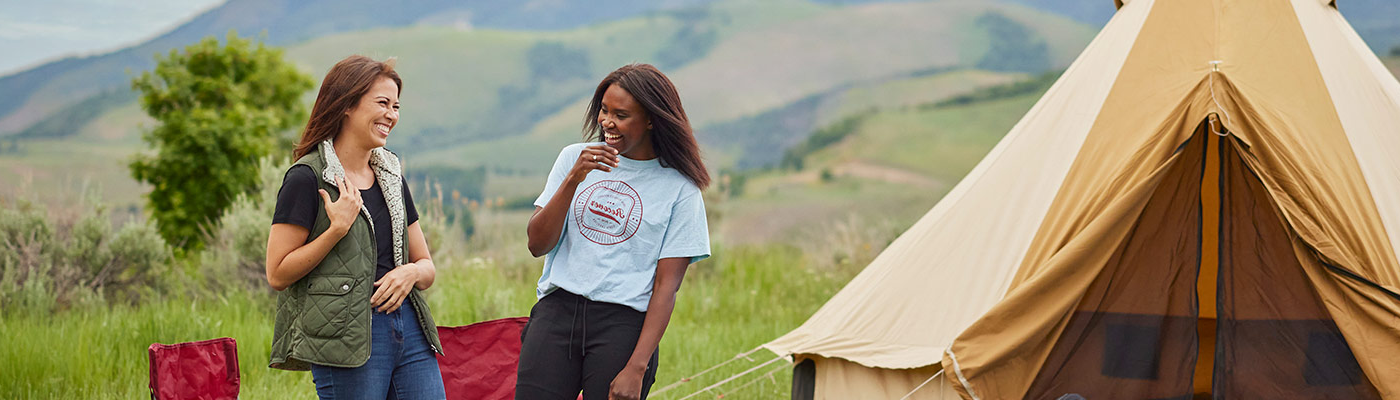 Two women laugh together at their campsite featuring a Sierra Canvas Tent.
