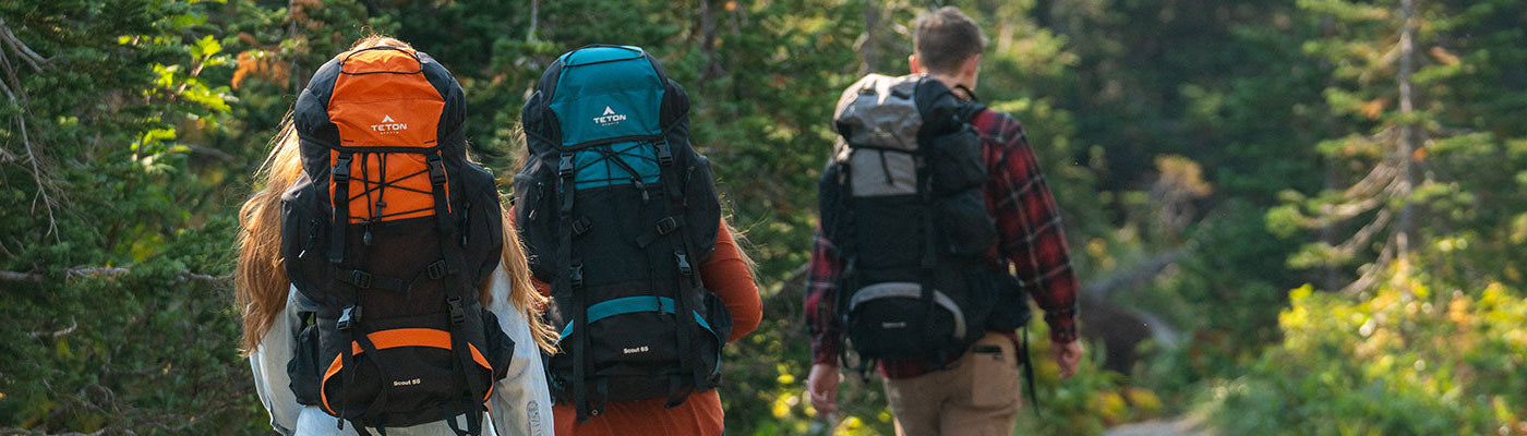 Three friends hiking through a forest with their Scout & Explorer packs.