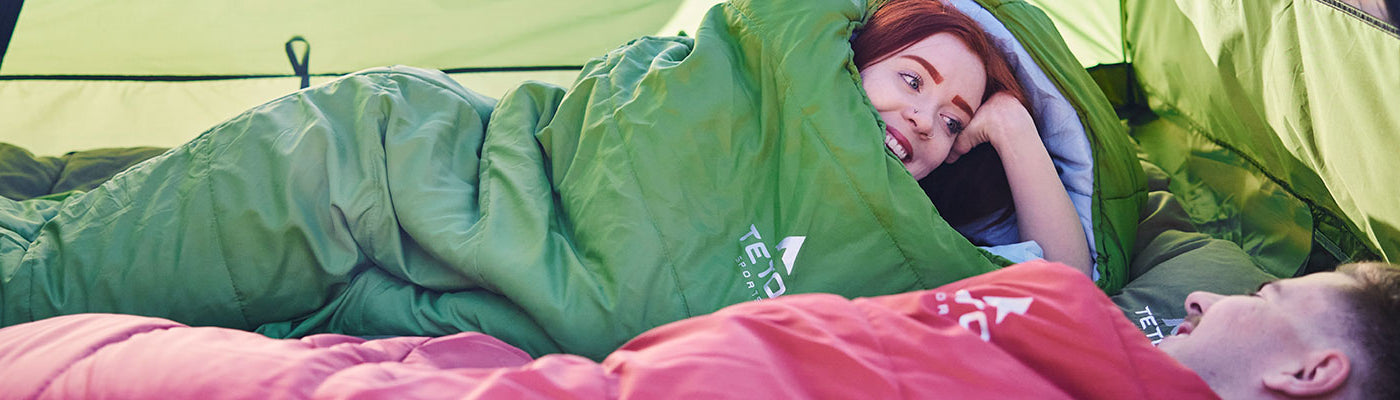 A couple snuggles together inside a TETON Sports Vista Tent while using their Celsius XXL Sleeping Bags.