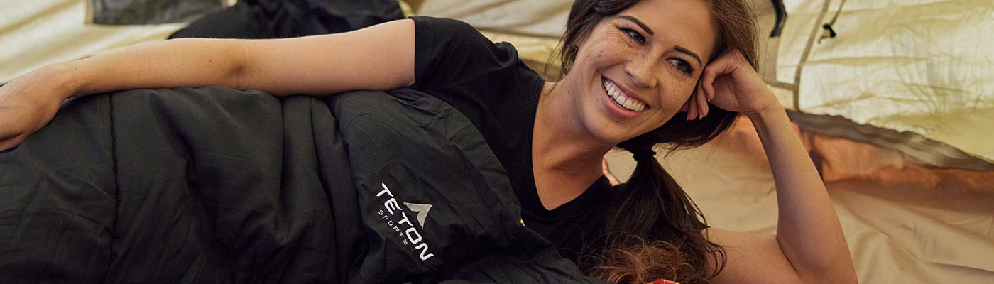 A couple snuggles together inside a TETON Sports Mountain Ultra Tent and their Celsius Sleeping Bags.