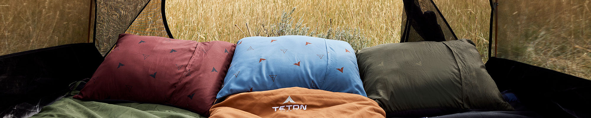 TETON Sports Grand Camp Pillows in three colors are shown laying with sleeping bags in a tent.