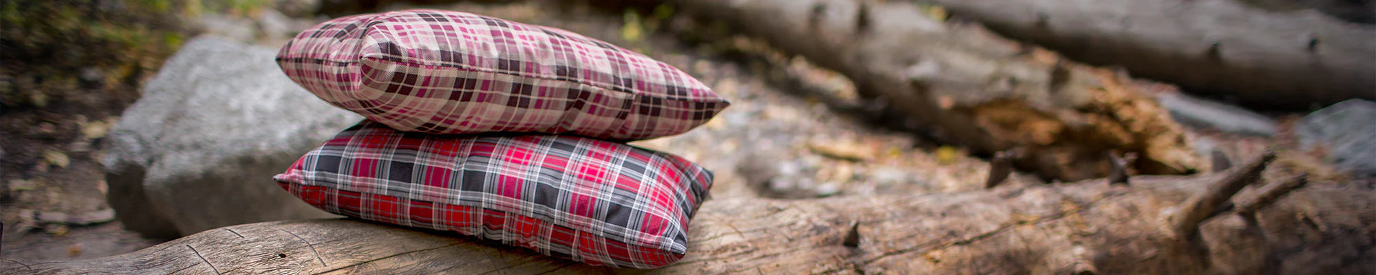 Two TETON Sports Camp Pillows sit on a log in a campsite.