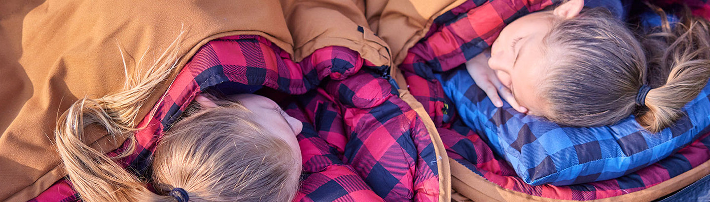 Two girls lay down in their TETON Sports sleeping bags with their head's on camp pillows.