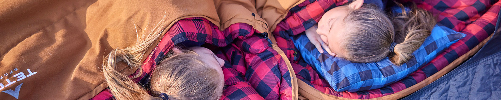 Two girls lay down in their TETON Sports sleeping bags with their head's on camp pillows.