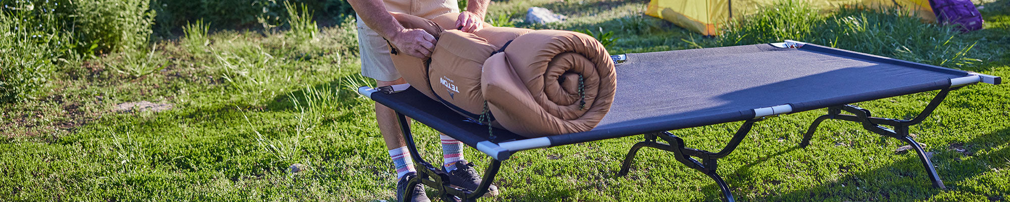 A man unbuckles his rolled up TETON Sports canvas camp pad atop his Outfitter XXL camp cot.