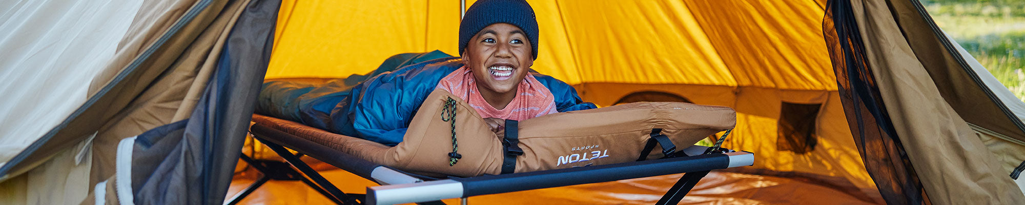A young boy lays on his TETON Sports Adventurer cot and camp pad while inside a Sierra Canvas Tent.
