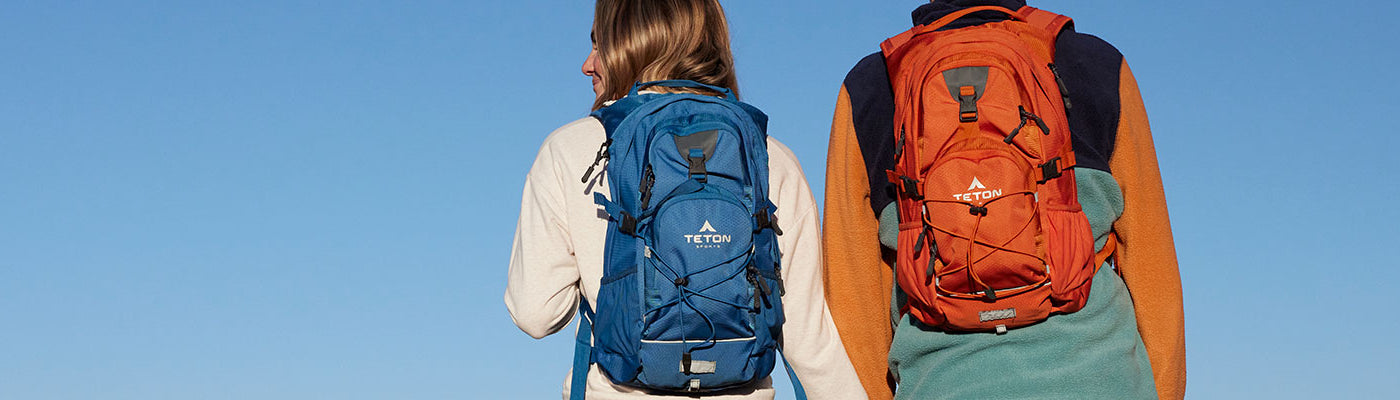 A man and a woman stand with their blue and orange Oasis hydration packs on their backs.