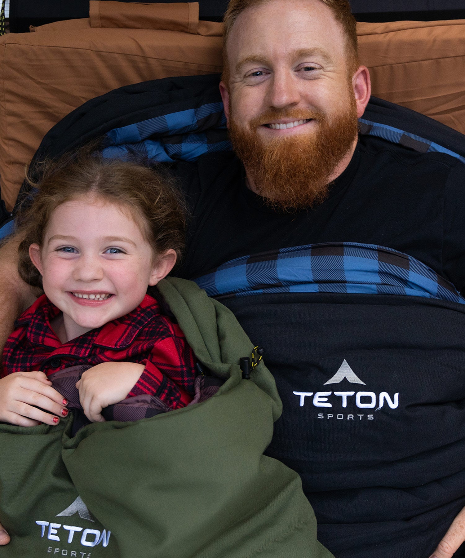 Image shows a man and child smiling while snuggled in two TETON Sports Bridger Canvas Sleeping Bags.