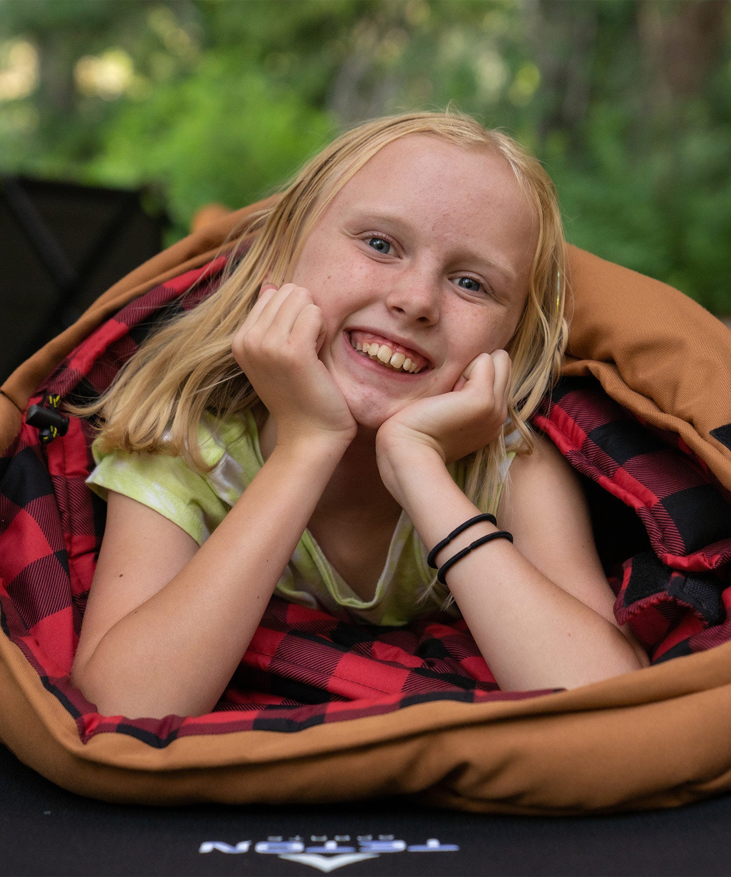 Image shows a young girl smiling while snuggled in a brown TETON Sports Bridger Canvas Sleeping Bag.
