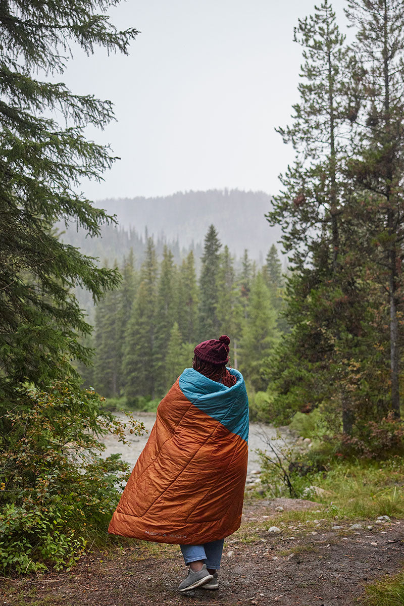 A woman in her camp blanket walking through a forest.