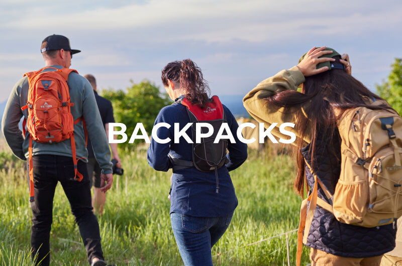 A group of friends hike through a green meadow with their TETON Sports Oasis and TrailRunner hydration packs.