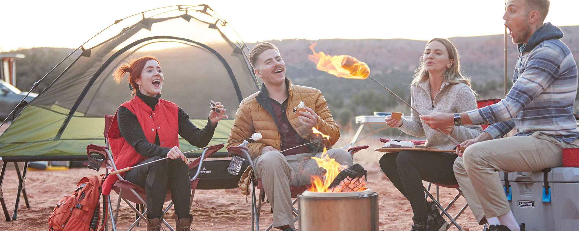 A group of four friends roast marshmallows surrounded by TETON Sports camping gear.