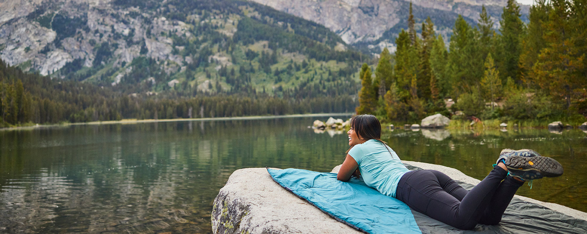 A woman laying on her blanket near a lake.